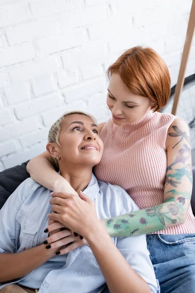 Tatoué femme câlin heureux lesbienne copine tout en regardant l'autre à la maison — Photo de stock