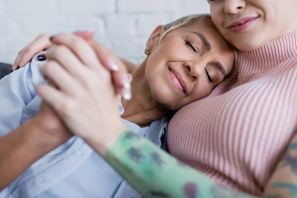 Happy lesbian woman with closed eyes holding hands with blurred girlfriend at home — Stock Photo