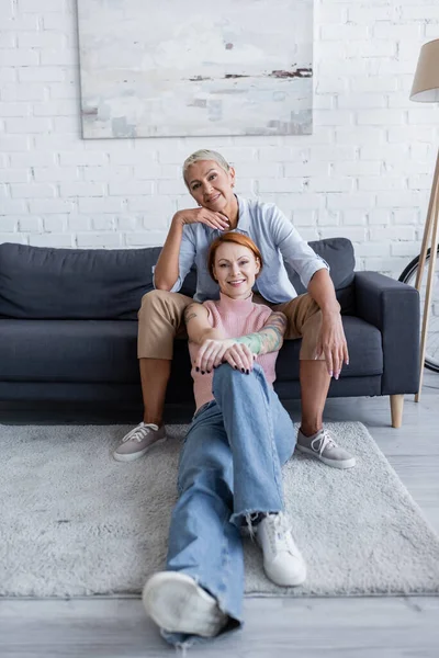 Complacido mismo sexo pareja mirando cámara en sala de estar - foto de stock