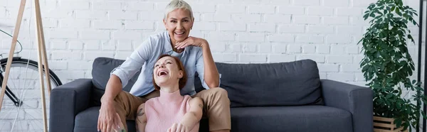 Smiling lesbian woman looking at camera near laughing girlfriend, banner — Stock Photo