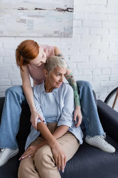 Tatoué femme câlin lesbienne copine regarder loin sur canapé à la maison — Photo de stock