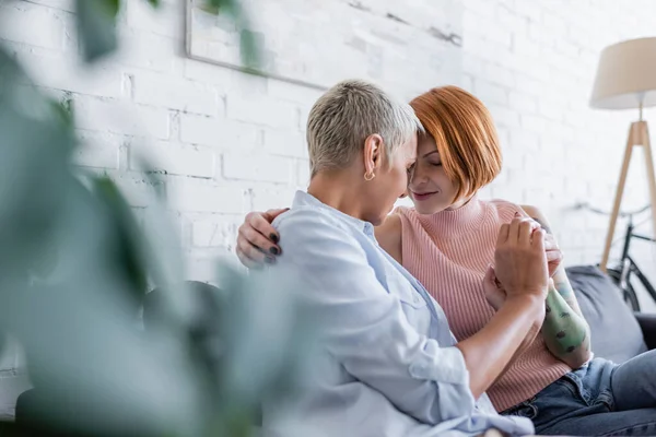 Happy lesbian women sitting face to face in living room on blurred foreground — Stock Photo