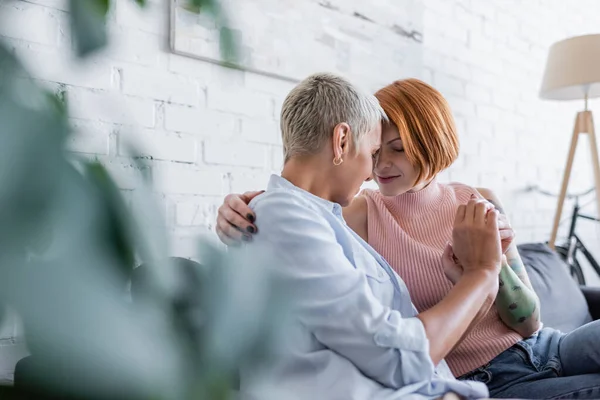 Heureux lesbiennes femmes assis face à face dans le salon sur flou au premier plan — Photo de stock