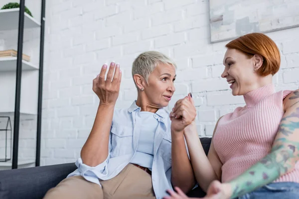 Alegre lesbianas mujeres cogidas de la mano durante la conversación en casa - foto de stock