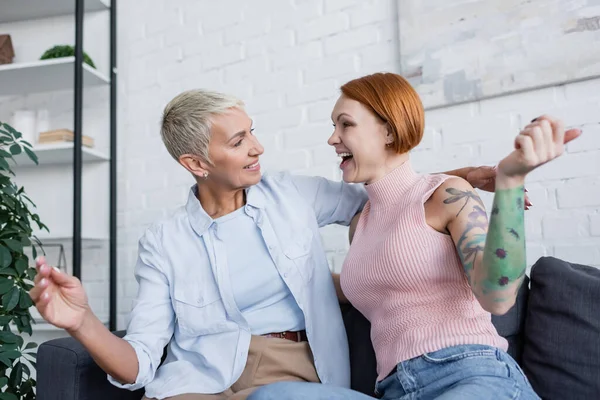 Excité lesbiennes femmes regardant les uns les autres tout en étant assis sur canapé dans le salon — Photo de stock