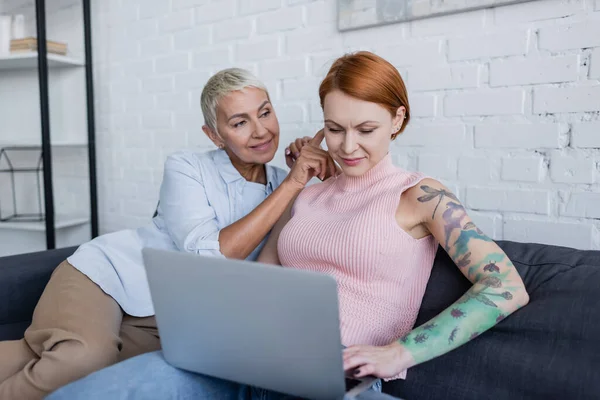 Lächelnde Frau sitzt neben lesbischer Freundin und arbeitet zu Hause am Laptop — Stockfoto