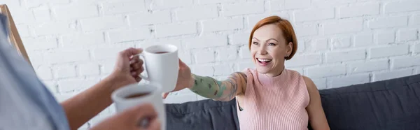 Femme floue tenant des tasses à thé près de petite amie lesbienne gaie, bannière — Photo de stock