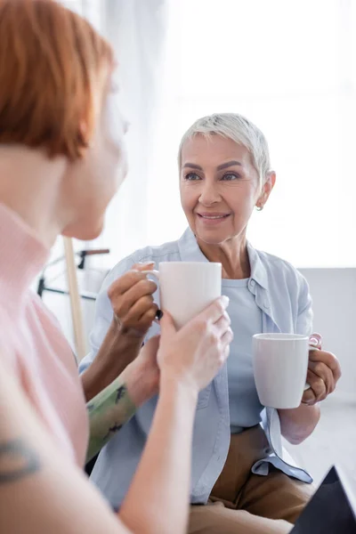 Borrosa mujer tomando taza de té de sonriente lesbiana novia - foto de stock