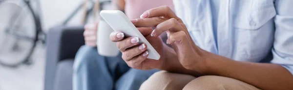 Abgeschnittene Ansicht einer lesbischen Frau mit Smartphone in der Nähe einer verschwommenen Freundin zu Hause, Banner — Stockfoto