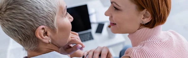 Glückliche lesbische Frauen, die einander in der Nähe verschwommener Gadgets zu Hause anschauen, Banner — Stockfoto