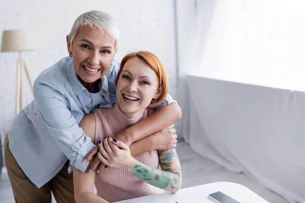 Excité et heureux couple lesbien regardant caméra à la maison — Photo de stock