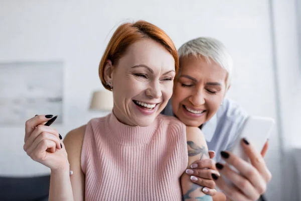 Rire femme tenant flou smartphone près joyeuse lesbienne petite amie — Photo de stock