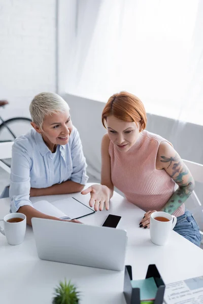 Découragée femme pointant vers ordinateur portable près de sourire lesbienne copine — Photo de stock