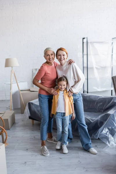 Full length vista de casal lésbico com a filha adotada sorrindo para a câmera no novo apartamento — Fotografia de Stock