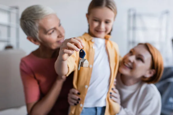 Blurred girl holding key from new apartment near same sex parents — Stock Photo