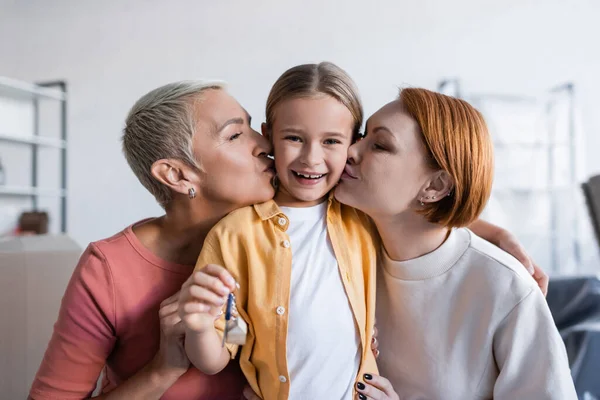 Same sex couple kissing happy adopted daughter holding key from new apartment — Stock Photo