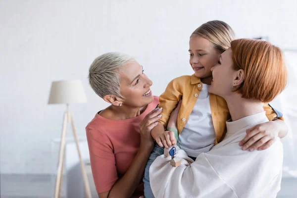 Bambino sorridente che tiene la chiave dal nuovo appartamento vicino alle madri felici dello stesso sesso — Foto stock