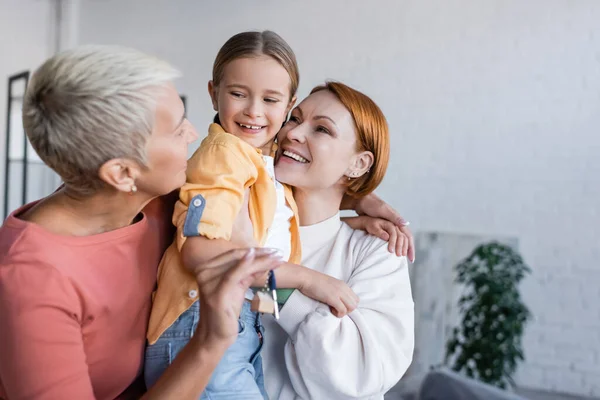 Femme lesbienne floue tenant la clé du nouvel appartement près de petite amie et fille adoptive — Photo de stock