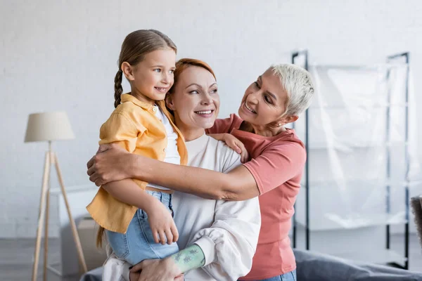 Allegra donna lesbica abbracciando fidanzata con figlia adottiva in nuova casa — Foto stock