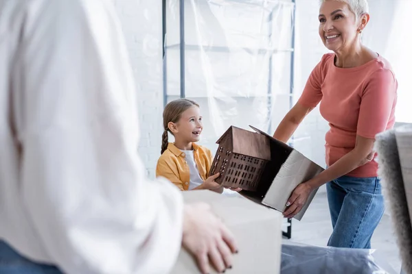 Веселый ребенок держит модель дома рядом с однополыми родителями с коробками — стоковое фото