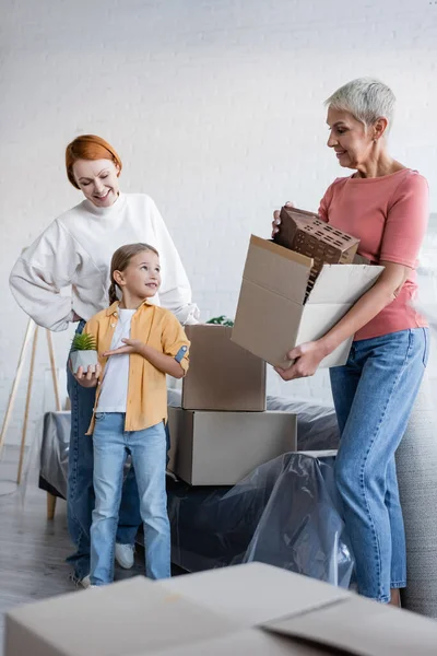 Lesbienne femme holding box avec maison modèle près adopté fille pointant à flowerpot — Photo de stock