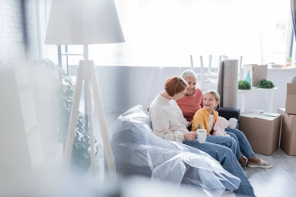 Lesbiana pareja sentado en sofá en nuevo apartamento con feliz adoptiva hija - foto de stock