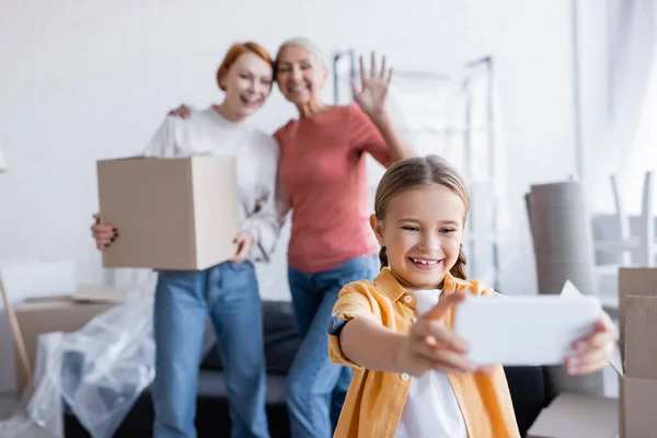 Ragazzo positivo con videochiamata su smartphone vicino alle madri con scatola di cartone a casa — Foto stock