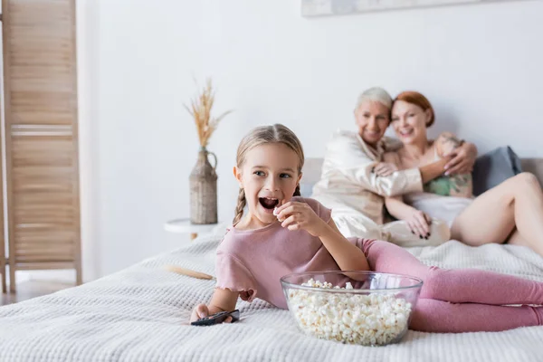 Kid holding popcorn while watching film near mothers on bed — Stock Photo
