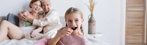 Enfant tenant du pop-corn près de parents lesbiennes flous sur le lit, bannière — Photo de stock