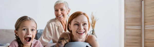 Excited kid looking away near lesbian mothers on bed, banner — Stock Photo