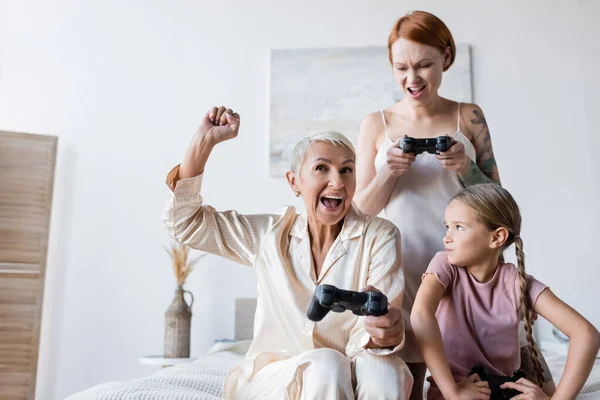 KYIV, UKRAINE - DECEMBER 8, 2021: Excited lesbian woman holding joystick near girlfriend and kid at home — Stock Photo