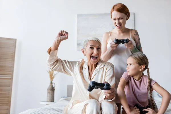 KYIV, UCRANIA - 8 de diciembre de 2021: Mujer lesbiana emocionada sosteniendo el joystick cerca de la novia y el niño en casa - foto de stock