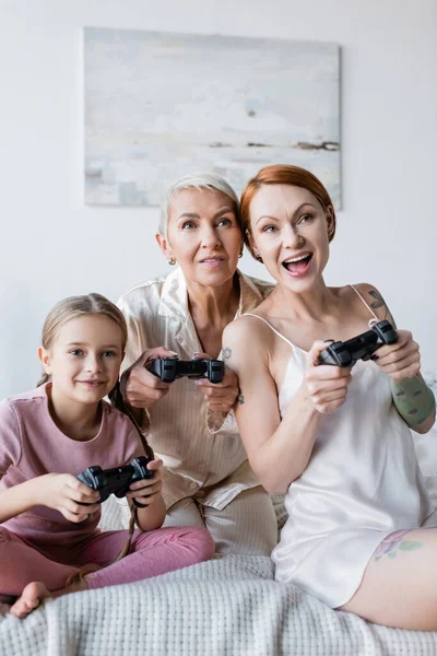 KYIV, UKRAINE - DECEMBER 8, 2021: Girl playing video game with moms on bed at home — Stock Photo