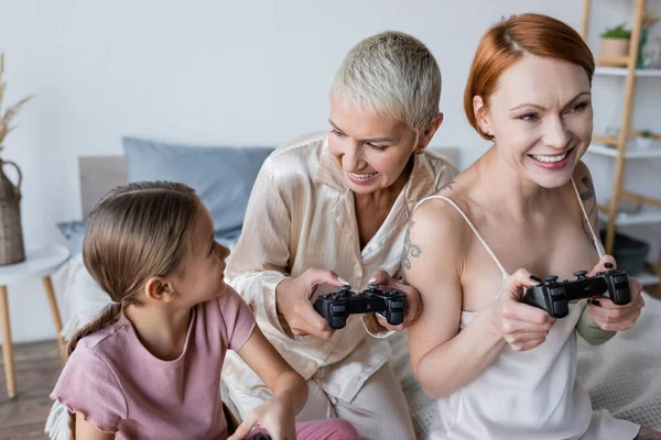 KIEW, UKRAINE - 8. DEZEMBER 2021: Lesbisches Paar spielt Videospiel neben Tochter im Schlafzimmer — Stockfoto