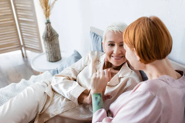 Lächelnde Frau im Schlafanzug hält Hand ihrer Freundin zu Hause auf dem Bett — Stockfoto