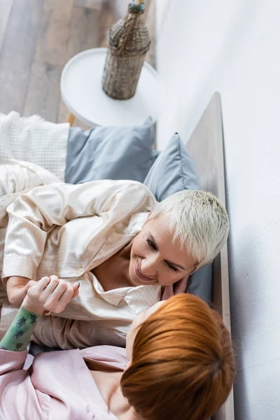 Vista aérea de mujeres lesbianas cogidas de la mano en la cama en casa - foto de stock