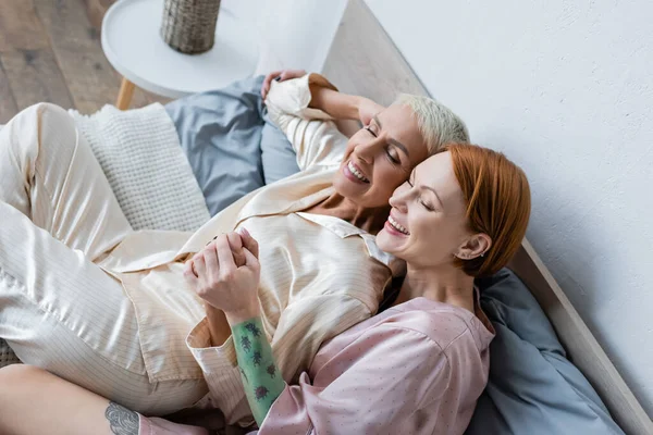 Hochwinkelaufnahme einer lächelnden Frau, die die Hand ihrer Freundin auf dem Bett hält — Stockfoto