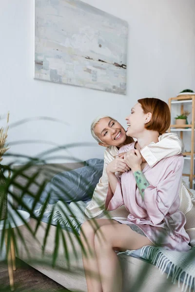 Улыбающаяся лесбиянка, обнимающая подружку в халате на кровати — стоковое фото