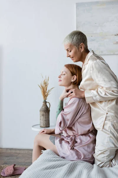 Smiling woman in pajamas holding hand of girlfriend on bed — Stock Photo