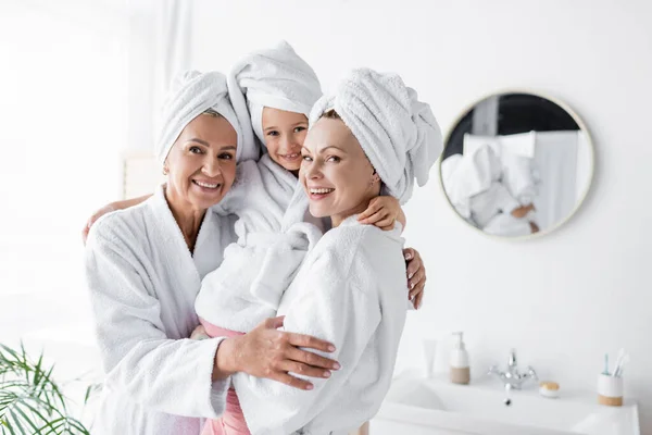 Positive lesbische Mütter halten Kind im Bademantel im Badezimmer — Stockfoto