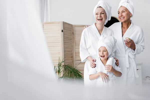 Cheerful lesbian couple and adopted daughter in bathrobes holding cosmetic cream in bathroom — Stock Photo