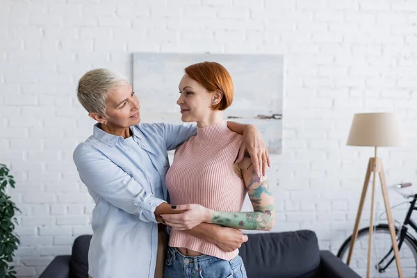 Sorrindo lésbica mulher abraçando tatuado namorada em casa — Fotografia de Stock