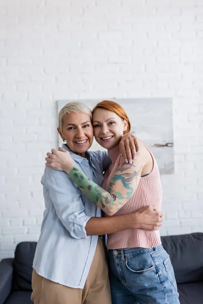 Casal de lésbicas abraçando e sorrindo para a câmera em casa — Fotografia de Stock