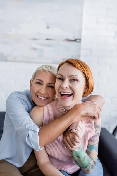 Smiling woman hugging tattooed girlfriend on couch at home — Stock Photo