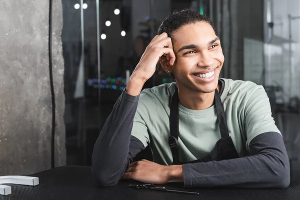 Joyeux toiletteur afro-américain regardant loin tout en étant assis dans le salon de toilettage — Photo de stock