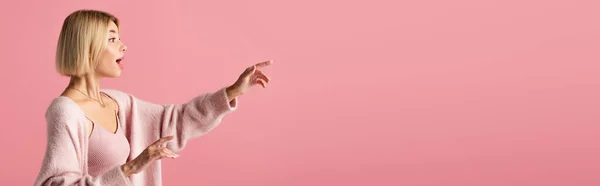 Vista lateral da jovem mulher chocada em casaco de lã macio olhando para longe e gesto isolado em rosa, banner — Fotografia de Stock