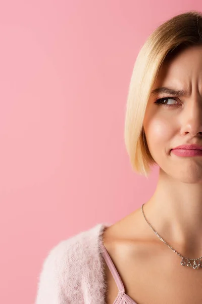 Vista recortada de la joven incierta frunciendo el ceño y mirando hacia otro lado aislado en rosa - foto de stock