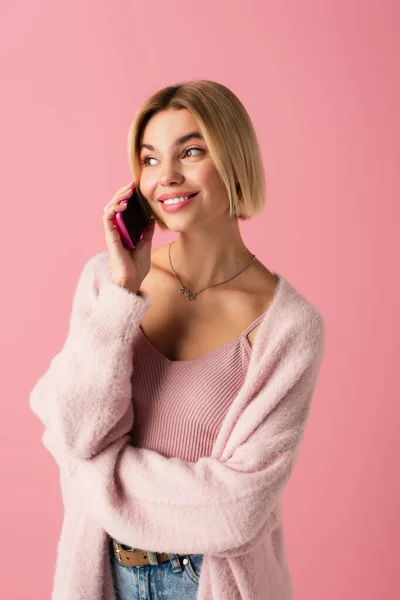 Glückliche junge Frau in weicher Strickjacke, die auf dem Smartphone isoliert auf rosa — Stockfoto