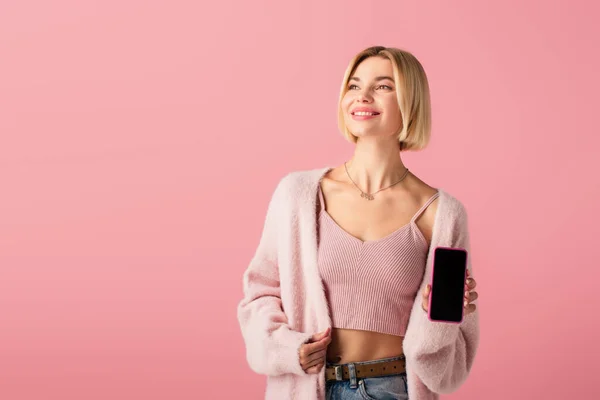 Positive young woman in soft cardigan holding smartphone with blank screen isolated on pink — Stock Photo