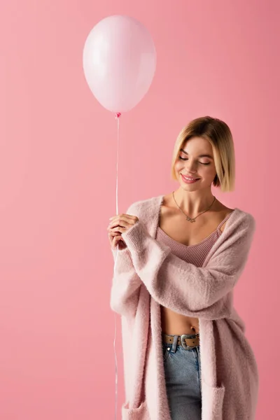 Compiaciuta giovane donna in cardigan tenuta palloncino isolato su rosa — Foto stock